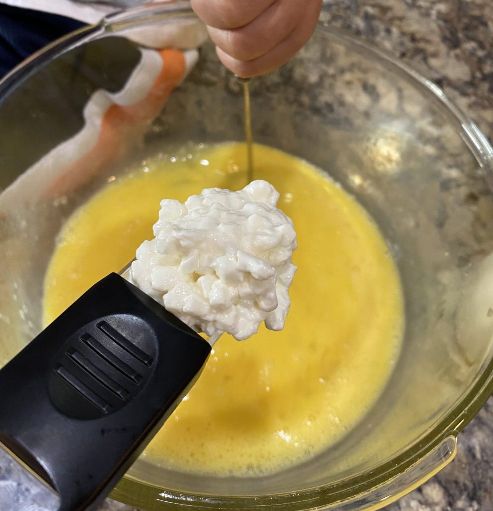 adding cottage cheese to a bowl of eggs